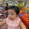 Kai Yumi joined the competition — help win amazing prizes! toddler, child, shopping_cart, grocery_store, fruit, oranges, bananas, woman, person, supermarket, aisle, clothing, pink_top, hair, earrings, shopping, retail, indoor, curious, baby