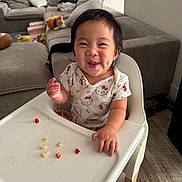 Kai Yumi is registered to the contest to win money with this photo: toddler, child, high_chair, food, smile, dimples, hello_kitty, shirt, indoor, living_room, sofa, toy, couch, floor, wood_floor, happy, person, furniture, cute, eating