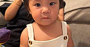 Kai Yumi is registered to the contest to win money with this photo: baby, child, infant, portrait, sitting, indoors, couch, overalls, white_clothing, dark_hair, spiky_hair, wide_eyes, looking_at_camera, face, hands, toy, adult, home, soft_lighting, photography