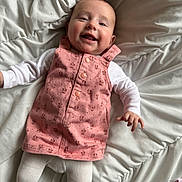 Lou a rejoint le concours — aidez-le/la à gagner de superbes lots ! baby, smiling, pink_dress, white_tights, lying_down, bed, comforter, infant, happy, child, portrait, cute, indoors, soft_lighting, fabric, clothing, person, face, hand, head