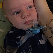 Cohen is registered to the contest to win money with this photo: baby, infant, face, hand, pacifier, onesie, blue_clothing, tattoo, bracelet, sea_creatures, closeup, indoor, person, child, portrait, cute, newborn, expression, looking_away, soft_lighting