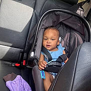 Amiri is registered to the contest to win money with this photo: baby, car_seat, child, infant, blue_clothing, car_interior, leather_seat, seatbelt, purple_jacket, safety, portrait, young_child, cute, looking_at_camera, seat, car_backseat, daylight, window, child_safety, car_trip