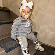 Hailey participe au concours pour gagner de l'argent avec cette photo : adidas, blue_eyes, bow, carpet, casual, child, curious, geometric_wall, gray_clothing, headband, indoor, nike, pacifier, portrait, seated, sneakers, socks, stairs, toddler, tracksuit