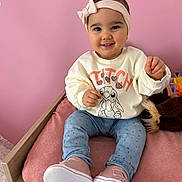 Lyana participe au concours pour gagner de l'argent avec cette photo : child, toddler, baby, headband, pink_background, smile, sitting, shoes, sweatshirt, jeans, cushion, plush_toy, wooden_bed, nursery, cozy, portrait, rosy_cheeks, indoors, cute, happy