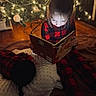 baby, blanket, book, child, christmas_tree, cozy, family, festive, floor, holiday, indoors, night_time, pajamas, reading, red_and_black_checkered, relaxation, sleeping_baby, soft_light, warm_lighting, wooden_floor