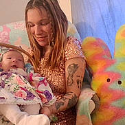 Serenity joined the competition — help win amazing prizes! baby, blanket, chair, child, cozy, cute, family, floral_dress, happy, holding, indoor, person, plush_toy, portrait, rainbow_colors, sequin_shirt, smiling, tattoos, woman, young
