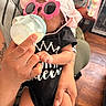 Kennedi joined the competition — help win amazing prizes! baby, bottle, sunglasses, pink_hat, black_clothing, adult_hand, tattoo, indoor, wooden_floor, framed_pictures, feeding, infant, cute, holding, person, fashion_accessory, relaxing, casual, home, comfort