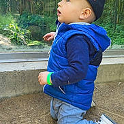 Malow participe au concours pour gagner de l'argent avec cette photo : child, toddler, kid, baseball_cap, blue_jacket, puffer_vest, kneeling, sneakers, dirt, outdoor, park, glass_panel, greenery, plants, curious, profile_view, wristband, jeans, young_child, muddy_clothes