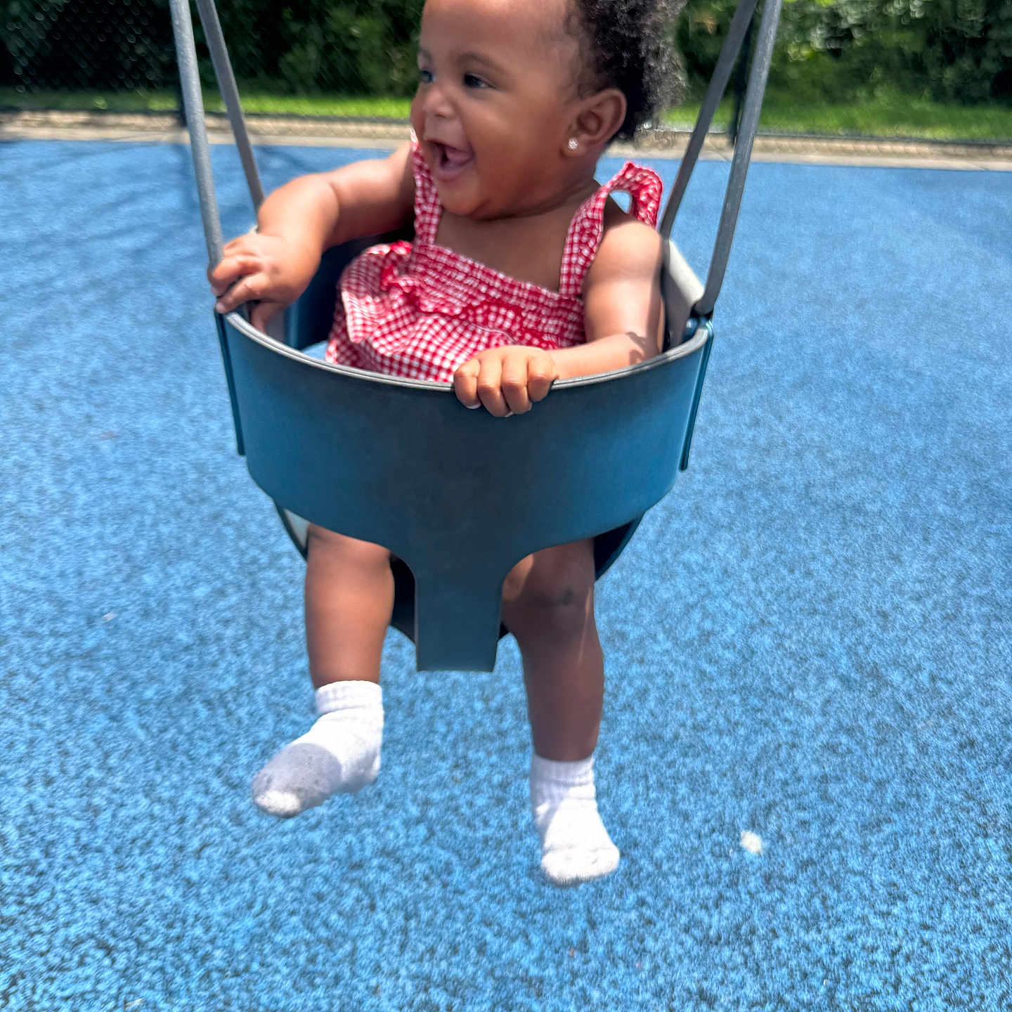 Malaya joined the competition — help win amazing prizes! toddler, child, swing, playground, outdoor, smiling, happy, curly_hair, red_clothing, white_socks, blue_floor, baby_swing, sunlight, greenery, park, fun, joy, summer, play, person