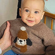 Jules a rejoint le concours — aidez-le/la à gagner de superbes lots ! baby, toddler, child, sweater, dog_motif, jeans, hands, chair, wooden_chair, portrait, smile, blue_eyes, indoor, cozy, knitwear, person, looking_at_camera, seated, grandparent_hand, cute