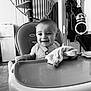 baby, high_chair, blanket, smiling, indoor, kitchen, spiral_staircase, black_and_white, child, face, person, furniture, door, appliance, happy, seat, toy, table, home, infant
