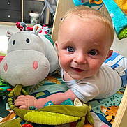 Clément participe au concours pour gagner de l'argent avec cette photo : baby, child, playmat, plush_toy, hippopotamus_toy, green_toy, smiling, blue_eyes, white_shirt, indoor, floor_play, wooden_frame, colorful, cute, soft_toys, infant, happy, closeup, person, crawling