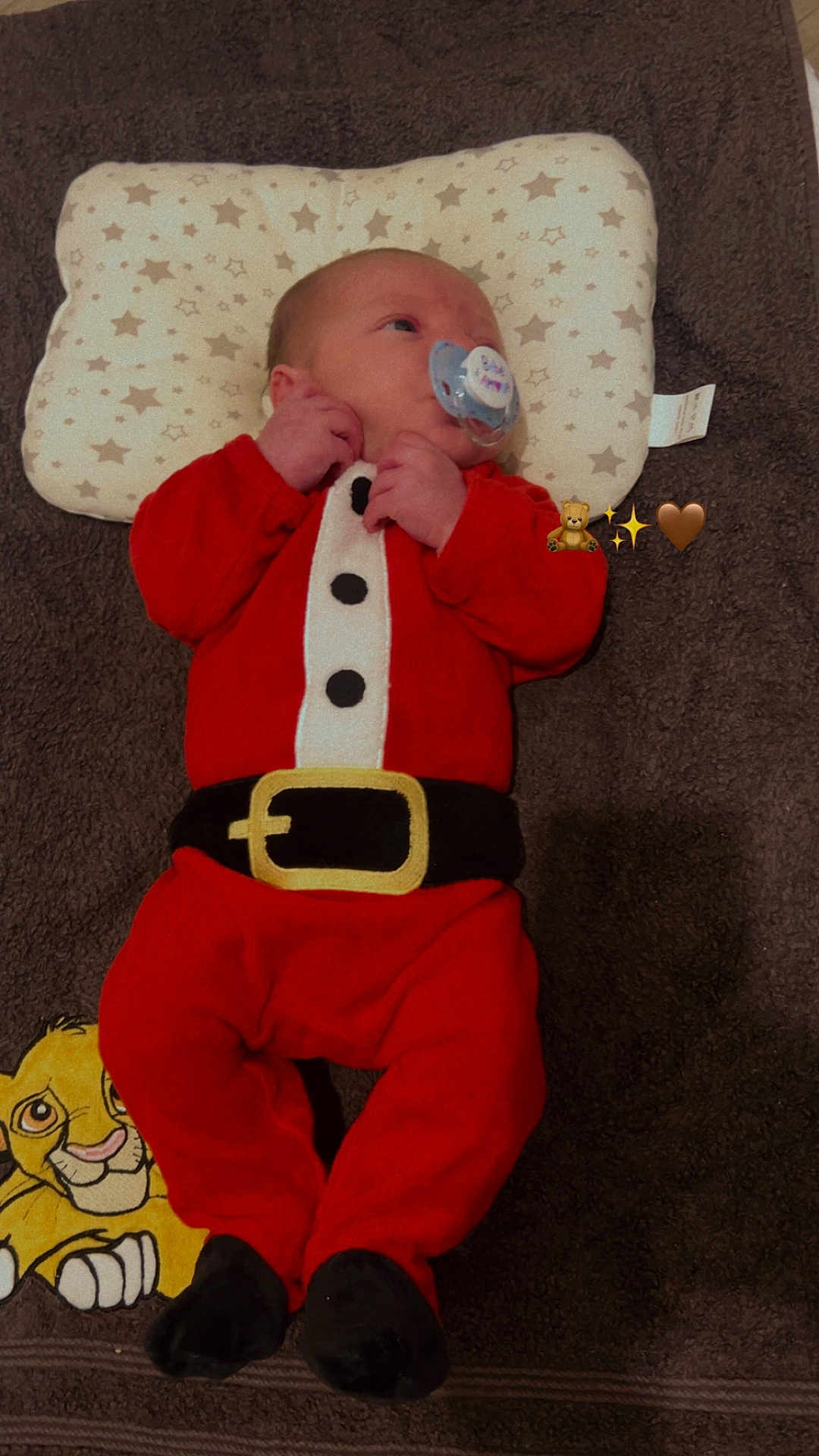 Gabriel a rejoint le concours — aidez-le/la à gagner de superbes lots ! baby, infant, pacifier, red_clothing, santa_outfit, pillow, star_pattern, blanket, cartoon_lion, lying_down, cute, indoors, sleepwear, child, soft_toys, holiday_theme, emojis, closeup, comfortable, peaceful