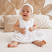 Ninon a rejoint le concours — aidez-le/la à gagner de superbes lots ! baby, bed, blue_eyes, child, cozy, cute, decor, happy, headband, homedecor, indoor, infant, leaf_pattern, pillows, portrait, sitting, smiling, soft_light, texture, white_dress