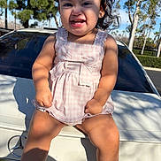 Mylani is registered to the contest to win money with this photo: child, toddler, smiling, pink_dress, bow, curly_hair, sitting, car_trunk, white_car, mercedes_logo, sunny, outdoor, trees, parking_lot, shoes, socks, playful, baby_teeth, portrait, shadow