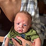 Zakari joined the competition — help win amazing prizes! baby, infant, child, portrait, face, eyes, wide_eyed, sitting, being_held, green_shirt, blanket, plaid, tattoo, hand, adult, indoor, close_up, photography, cozy, family
