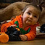 baby, black_decoration, blanket, child, cozy, cute, face, festive, floor, halloween, haystack, holiday, indoors, lying_down, orange_clothing, person, portrait, pumpkin_outfit, toddler, toy