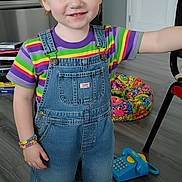 Aurora is registered to the contest to win money with this photo: child, red_hair, headband, overalls, striped_shirt, colorful_clothing, socks, sneakers, toy_phone, floor, room, door, poster, bracelet, smile, standing, indoor, playful, happy, person
