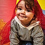 toddler, child, smile, face, striped_clothing, hoodie, red_scarf, crawling, colorful_background, yellow, red, blue, playmat, curly_hair, cute, indoors, happy, portrait, baby, person