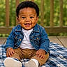 baby, smiling, denim_jacket, white_shirt, khaki_pants, blue_blanket, outdoor, wooden_fence, greenery, happy, cute, sitting, child, portrait, casual_clothing, feet, shoes, curly_hair, infant, daylight