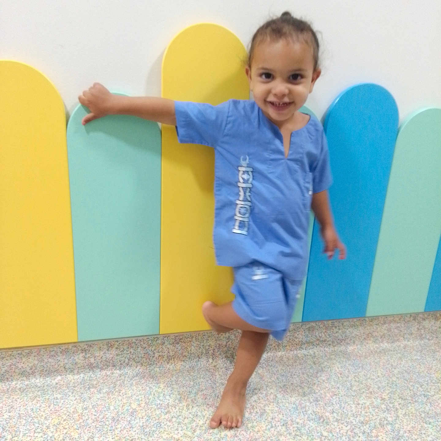 Jilyan a rejoint le concours — aidez-le/la à gagner de superbes lots ! barefoot, blue_clothing, casual, child, colorful_background, cute, floor, fun, happy, indoor, joyful, pastel_colors, person, playful, posing, scrubs, small_child, smiling, wall, young