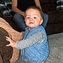 toddler, child, man, tattoo, couch, carpet, blue_vest, gray_clothing, polka_dot, living_room, furniture, person, indoor, family, curious, standing, casual, home, portrait, cozy