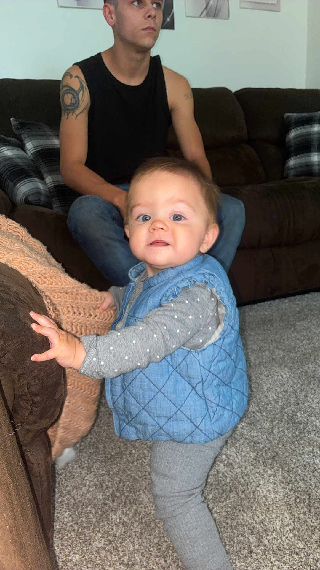 November joined the competition — help win amazing prizes! toddler, child, man, tattoo, couch, carpet, blue_vest, gray_clothing, polka_dot, living_room, furniture, person, indoor, family, curious, standing, casual, home, portrait, cozy