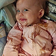 Myla is registered to the contest to win money with this photo: baby, child, infant, smiling, portrait, indoors, sitting, reclining, pink_outfit, giraffe_pattern, pajamas, blanket, pillow, couch, home, face, eyes, blonde_hair, happy, closeup