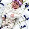 baby, blanket, clothing, cute, flower, grass, headband, headwear, infant, lying_down, nature, outdoor, patterned_pants, portrait, purple, relaxed, socks, soft_light, white_shirt, young_child