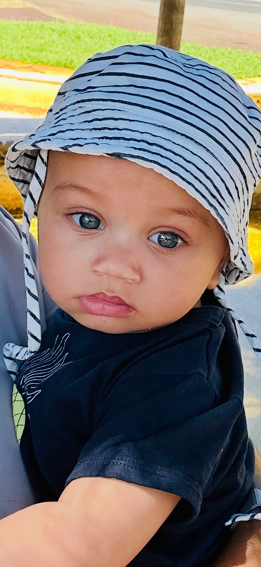 Ellis a rejoint le concours — aidez-le/la à gagner de superbes lots ! toddler, child, hat, striped_hat, black_shirt, face, eyes, outdoor, daylight, tree, grass, portrait, close_up, expression, baby, skin, person, headwear, summer, cute