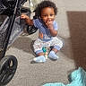 Marcellus joined the competition — help win amazing prizes! baby, blanket, blue_shirt, carpet, child, curly_hair, cute, floor, hand, indoor, patterned_pants, person, playtime, shadow, sitting, smiling, stroller, sunlight, toy, young_child