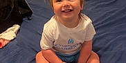 Aria a rejoint le concours — aidez-le/la à gagner de superbes lots ! toddler, child, smiling, sitting, bed, bedspread, indoor, pigtails, hair_ties, clothing, white_tshirt, blue_shorts, happy, face, person, room, bag, spray_bottle, casual, home