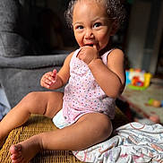 Mckenna is registered to the contest to win money with this photo: baby, barefoot, basket, blanket, child, close_up, curly_hair, hand_to_mouth, happy, home, indoor, natural_light, pink_clothing, polka_dots, portrait, sitting, smiling, toddler, toy, wicker_chair