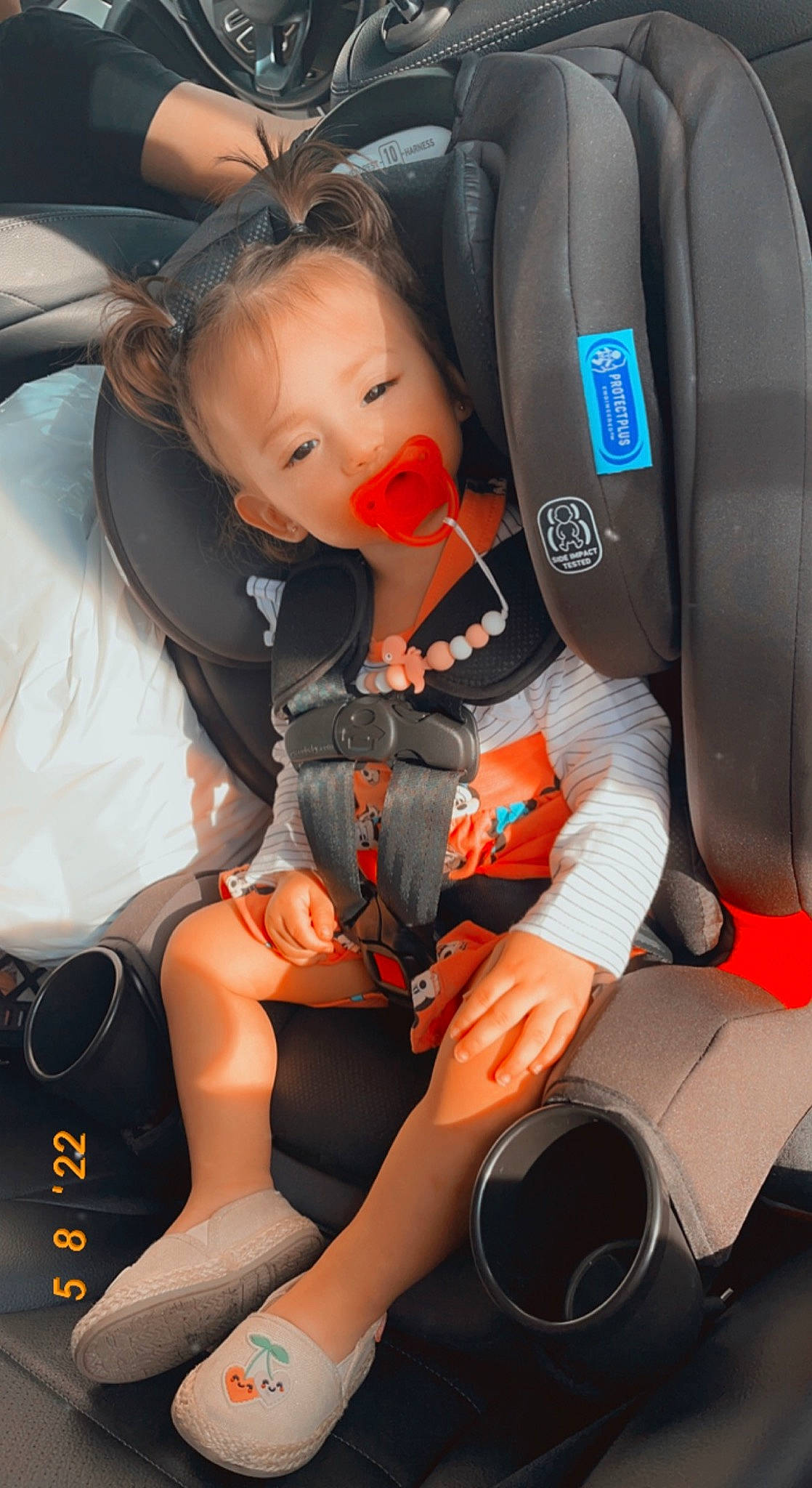 Ezlyn is registered to the contest to win money with this photo: automotive_design, baby_carriage, car, car_seat, car_seat_cover, comfort, knee, lap, leg, motor_vehicle, orange, person, seat_belt, shoe, sneakers, steering_part, steering_wheel, thigh, toddler, vehicle_door