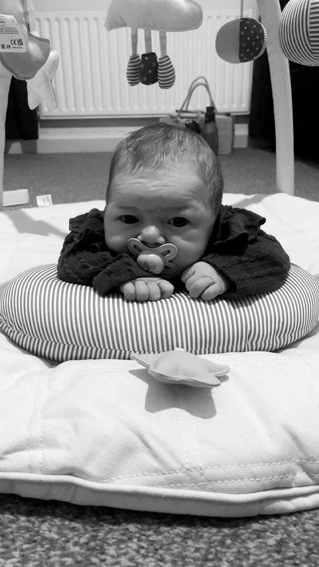 Cecelia-Nevaeh is registered to the contest to win money with this photo: baby, infant, pacifier, cushion, striped, soft_toys, blanket, floor, carpet, radiator, indoors, child, cute, lying_down, black_and_white, clothing, hands, head, face, room