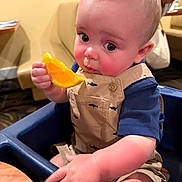 Bryer joined the competition — help win amazing prizes! adult, baby, background, bib, blue_clothing, child, citrus, eating, food, fruit, high_chair, indoor, infant, orange, overalls, portrait, restaurant, seated, table, wide_eyed