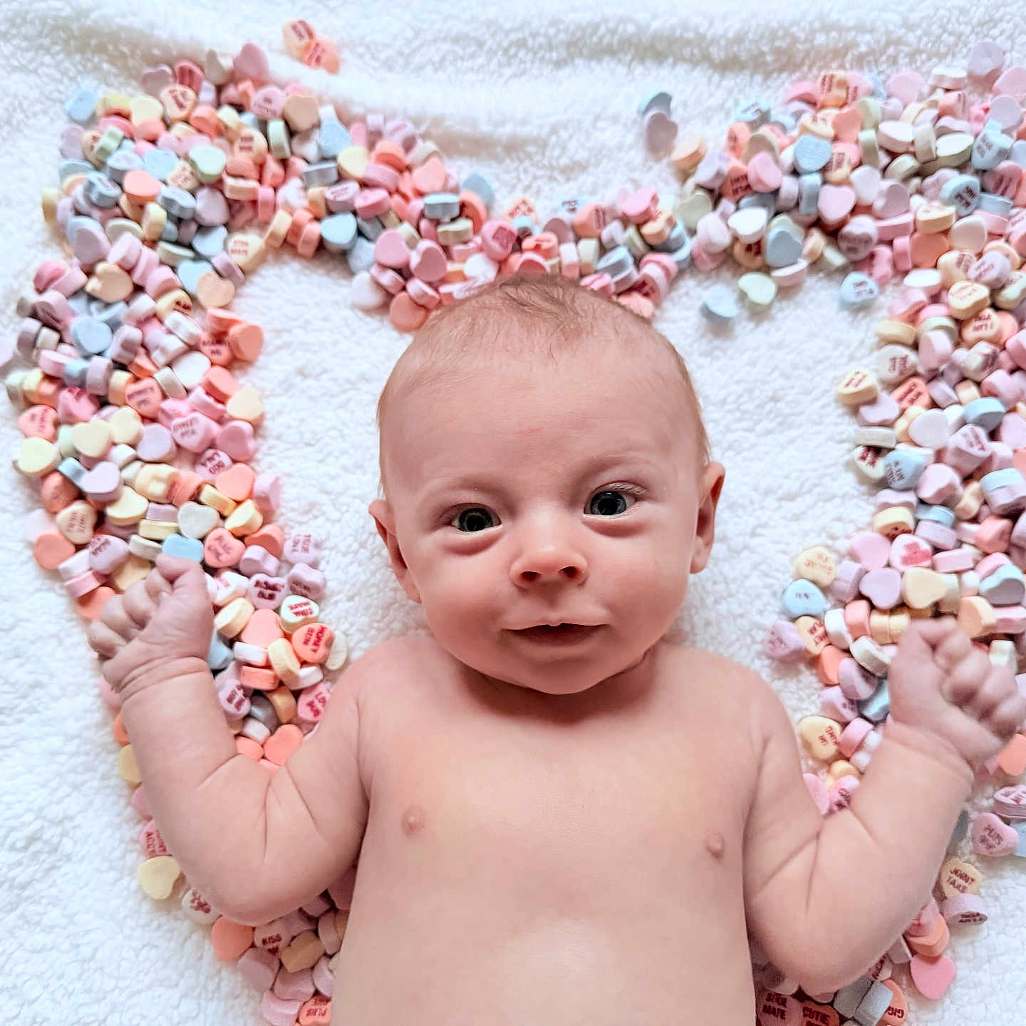Tucker is registered to the contest to win money with this photo: baby, bare_chest, blanket, candy, close_up, conversation_hearts, cute, eyes, hands, heart_shape, infant, lying_down, newborn, pastel_colors, playful, portrait, props, smile, soft_texture, valentine