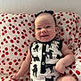 Nora is registered to the contest to win money with this photo: baby, smiling, onesie, dog_pattern, black_and_white, pillow, tomato_print, red, white, infant, happy, cute, indoor, child, headband, bow, sitting, face, skin, arm