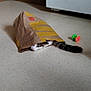 cat, paper_bag, kitchen_floor, wooden_cabinets, cat_toy, tail, floor, playful, hiding, domestic_cat, indoor, pet, curious, whiskers, striped_cat, tabby_cat, floor_tiles, household, animal, mischievous