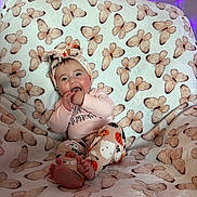 Everleigh is registered to the contest to win money with this photo: baby, child, infant, headband, pajamas, butterfly_pattern, blanket, sitting, happy, smiling, fingers_in_mouth, indoor, purple_lights, cozy, cute, face, feet, clothing, soft_texture, decor