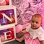 toddler, child, balloons, white_boxes, pink_skirt, carpet, decorative_lights, roses, pink_background, indoor, cute, sitting, baby, smiling, short_hair, playful, festive, party_decorations, bracelet, white_top