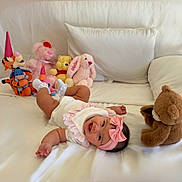 Valentina joined the competition — help win amazing prizes! baby, infant, pink_headband, white_outfit, stuffed_animals, teddy_bear, bunny, tiger, party_hat, bed, pillow, smiling, happy, lying_down, soft_toys, indoor, child, cute, playful, cozy