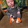baby, infant, child, sitting, armchair, couch, portrait, face, wide_eyed, neutral_expression, gray_outfit, patterned_clothing, orange_socks, indoors, furniture, cushion, blanket, colorful_background, autumn_colors, photography