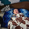baby, bed, blanket, blue, child, clothing, cow_print, cozy, crochet, elephant, face, happy, headboard, indoors, infant, lying_down, photograph, plush_toy, portrait, smiling