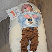 Eden a rejoint le concours — aidez-le/la à gagner de superbes lots ! baby, bear_design, blue_shirt, brown_pants, child, clothing, cozy, cute, fabric_background, indoor, infant, milestone_card, newborn, one_month, pacifier, person, resting, sleeping, soft_texture, white_cushion