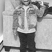 Maverick is registered to the contest to win money with this photo: child, smiling, standing, denim_jacket, sneakers, indoor, carpet, couch, hand_sign, happy, person, casual_clothing, portrait, young, fashion, hair, wall, footwear, jeans, cute