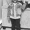 child, smiling, standing, denim_jacket, sneakers, indoor, carpet, couch, hand_sign, happy, person, casual_clothing, portrait, young, fashion, hair, wall, footwear, jeans, cute