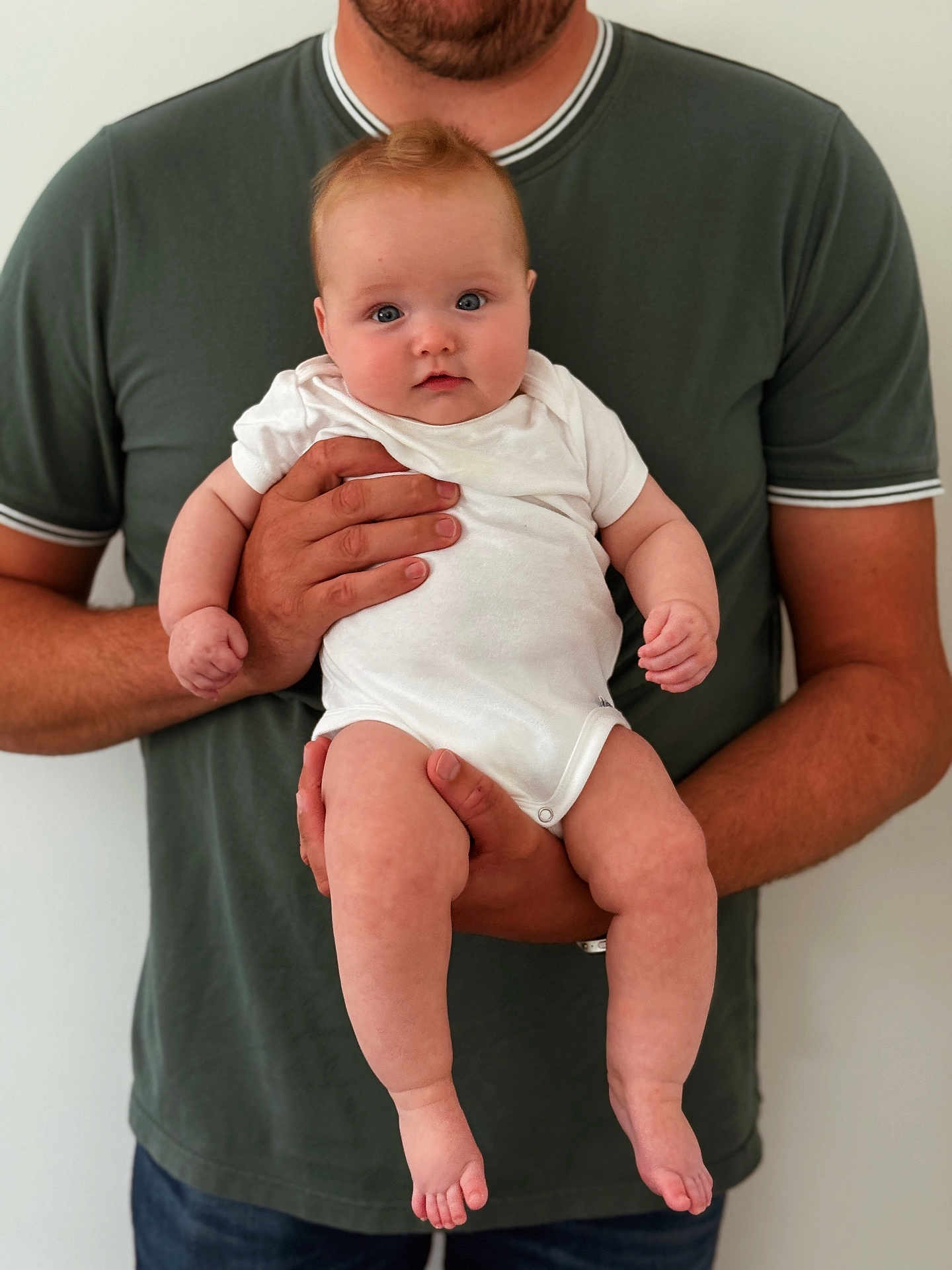 Blythe joined the competition — help win amazing prizes! baby, infant, child, person, adult, hands, white_onesie, green_shirt, blue_eyes, skin, portrait, holding, cute, indoor, casual_clothing, standing, human, parent, support, face