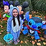 child, girl, costume, onesie, halloween, candy_bucket, inflatable, mickey_mouse, minnie_mouse, stitch, grass, leaves, outdoor, smiling, holiday, festive, yard, autumn, fun, celebration