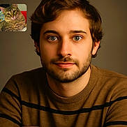 Bébé a rejoint le concours — aidez-le/la à gagner de superbes lots ! beard, brown_hair, casual, cat, closeup, communication, expression, face, feline, indoor, looking_at_camera, man, pet, portrait, striped_clothing, sweater, technology, video_call, warm_lighting, young_adult